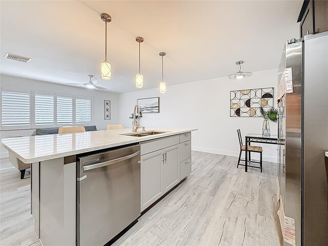 7125 S Shore Dr S, Saint Petersburg, FL 33707 - kitchen with appliances with stainless steel finishes, a sink, light wood-style floors, an island with sink, and pendant lighting