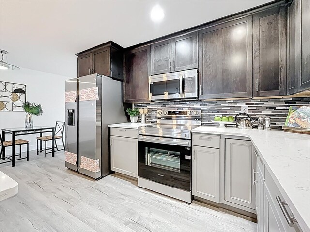 7125 S Shore Dr S, Saint Petersburg, FL 33707 - kitchen with stainless steel appliances, tasteful backsplash, dark brown cabinetry, light wood finished floors, and light stone counters