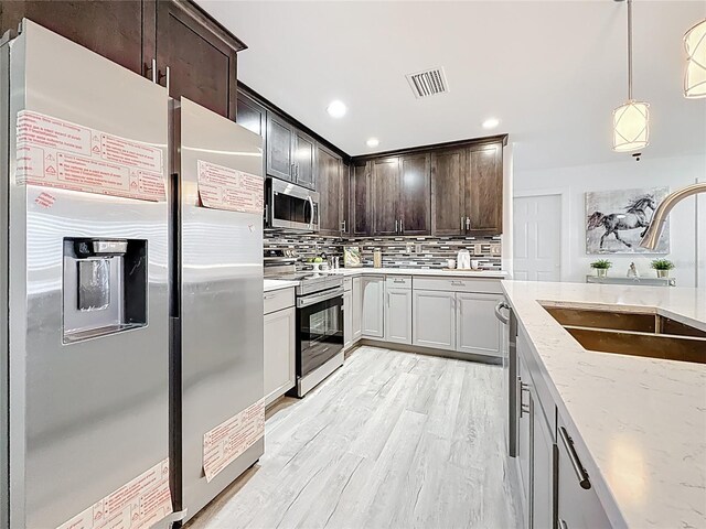 7125 S Shore Dr S, Saint Petersburg, FL 33707 - kitchen with appliances with stainless steel finishes, a sink, tasteful backsplash, dark brown cabinets, and light stone countertops