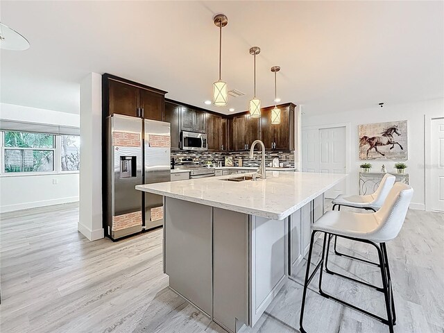 7125 S Shore Dr S, Saint Petersburg, FL 33707 - kitchen featuring appliances with stainless steel finishes, tasteful backsplash, light stone countertops, dark brown cabinets, and light wood-style flooring