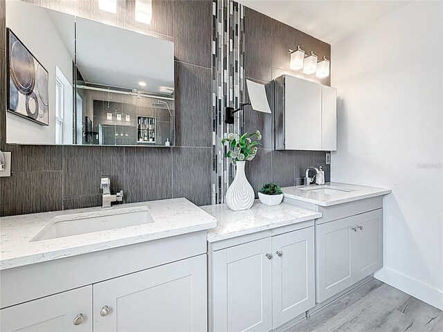 7125 S Shore Dr S, Saint Petersburg, FL 33707 - full bath featuring two vanities, a shower with shower door, wood finished floors, decorative backsplash, and baseboards