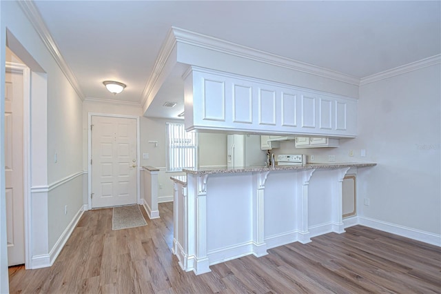 6550 Teak Ct, Zephyrhills, FL 33542 - kitchen with a peninsula, light wood-style floors, white appliances, a kitchen bar, and white cabinetry