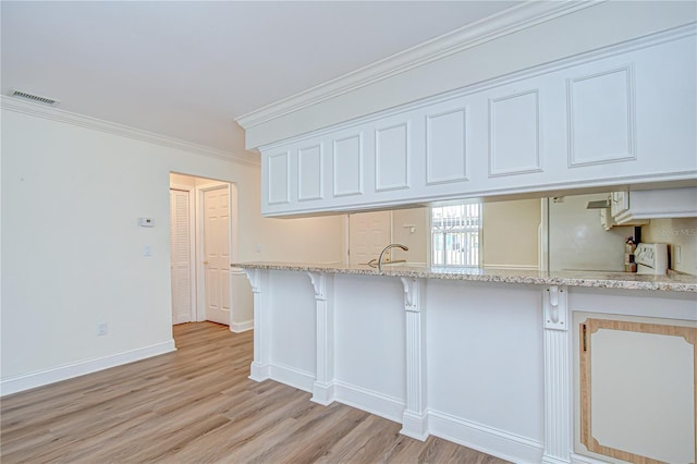 6550 Teak Ct, Zephyrhills, FL 33542 - kitchen with light wood-style flooring, a kitchen bar, light stone countertops, white cabinetry, and ornamental molding