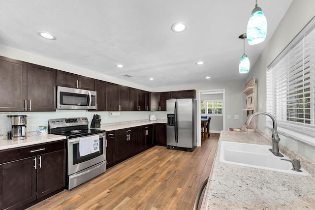 9591 Commodore Dr, Seminole, FL 33776 - kitchen with stainless steel appliances, a sink, dark brown cabinetry, decorative light fixtures, and light wood-type flooring