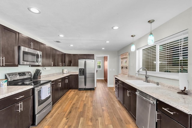 9591 Commodore Dr, Seminole, FL 33776 - kitchen with stainless steel appliances, a sink, dark brown cabinetry, light wood finished floors, and decorative light fixtures