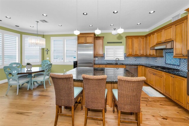 13303 Gulf Ln, Madeira Beach, FL 33708 - kitchen featuring appliances with stainless steel finishes, a sink, under cabinet range hood, brown cabinetry, and ornamental molding