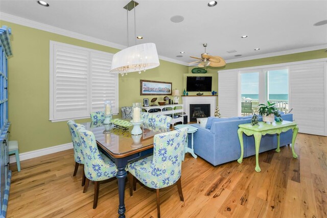 13303 Gulf Ln, Madeira Beach, FL 33708 - dining room featuring a ceiling fan, crown molding, baseboards, wood finished floors, and a glass covered fireplace