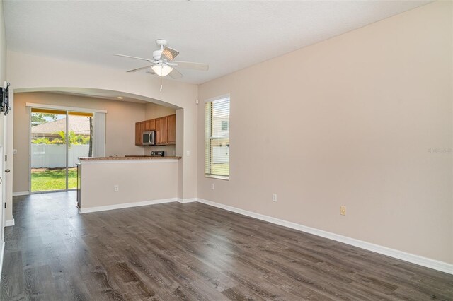 6920 Towering Spruce Dr, Riverview, FL 33578 - unfurnished living room featuring dark wood-style flooring, a ceiling fan, arched walkways, and baseboards