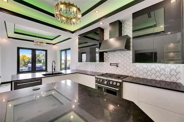 6526 Simone Shores Cir, Apollo Beach, FL 33572 - kitchen with a chandelier, wall chimney range hood, a sink, high end stainless steel range, and white cabinetry