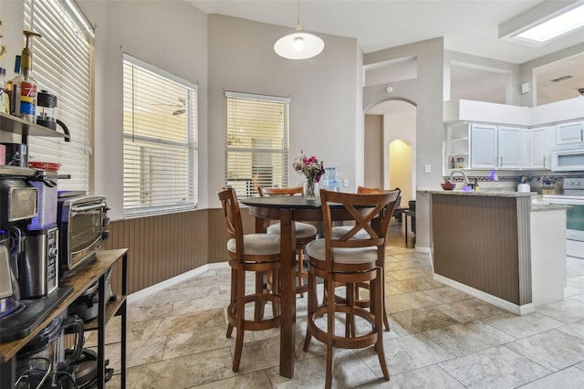 6918 Potomac Cir, Riverview, FL 33578 - dining room featuring arched walkways, high vaulted ceiling, a wainscoted wall, and stone tile floors