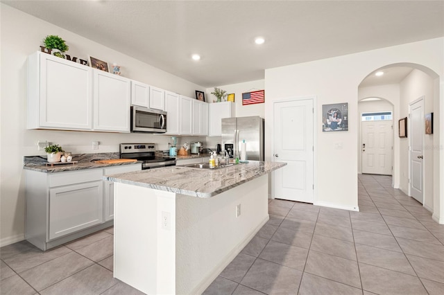 2925 Evergreen Elm Pass, Wesley Chapel, FL 33543 - kitchen featuring appliances with stainless steel finishes, light tile patterned flooring, white cabinets, arched walkways, and a kitchen island with sink