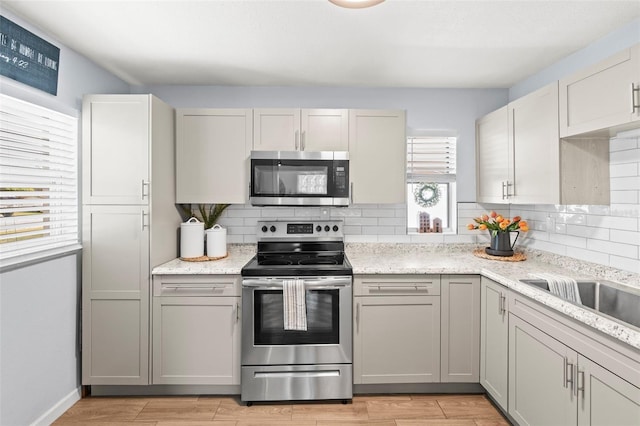 512 Flame Tree Dr, Apollo Beach, FL 33572 - kitchen with stainless steel appliances, backsplash, light wood-style flooring, and light stone countertops