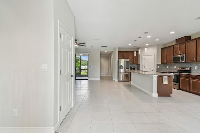 13311 Dorado Shores Ave, Riverview, FL 33579 - kitchen featuring appliances with stainless steel finishes, a sink, backsplash, light tile patterned floors, and a center island with sink