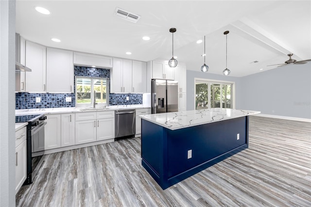9909 San Mateo Way, Port Richey, FL 34668 - kitchen featuring stainless steel appliances, a center island, white cabinetry, light stone countertops, and decorative backsplash
