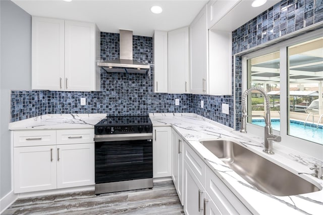 9909 San Mateo Way, Port Richey, FL 34668 - kitchen featuring range with electric cooktop, wall chimney range hood, a sink, white cabinetry, and recessed lighting