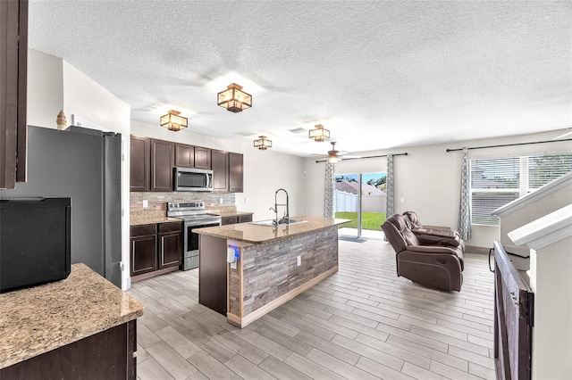 14135 Arbor Pines Dr, Riverview, FL 33579 - kitchen featuring appliances with stainless steel finishes, dark brown cabinets, ceiling fan, open floor plan, and light wood finished floors