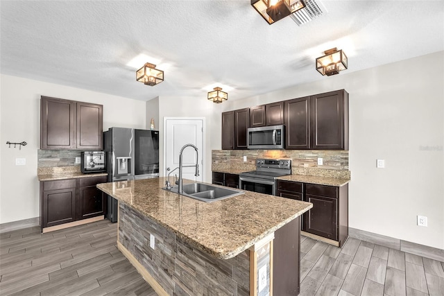 14135 Arbor Pines Dr, Riverview, FL 33579 - kitchen featuring appliances with stainless steel finishes, wood tiled floors, dark brown cabinetry, backsplash, and a kitchen island with sink