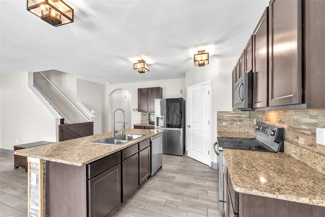14135 Arbor Pines Dr, Riverview, FL 33579 - kitchen featuring stainless steel appliances, backsplash, a center island with sink, dark brown cabinetry, and arched walkways