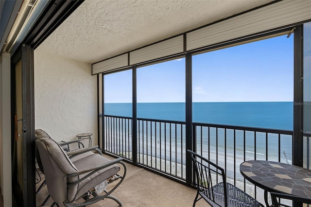 14950 Gulf Blvd Unit 905, Madeira Beach, FL 33708 - sunroom featuring a textured wall, view of water and beach, a textured ceiling, carpet flooring, and a wall of windows