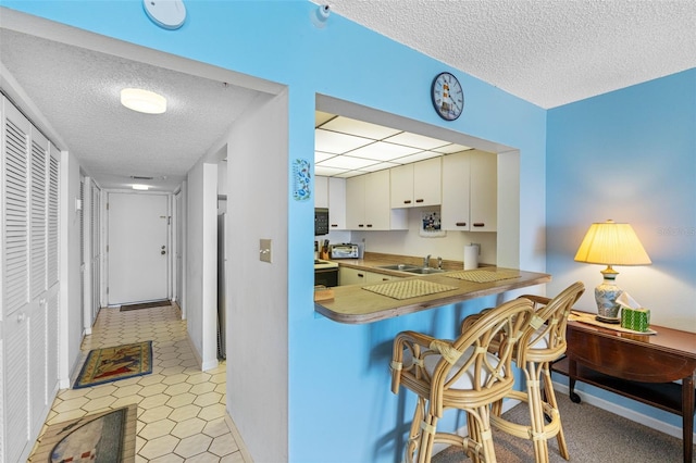 14950 Gulf Blvd Unit 905, Madeira Beach, FL 33708 - kitchen with a sink, a textured ceiling, a breakfast bar area, white cabinets, and light tile patterned flooring