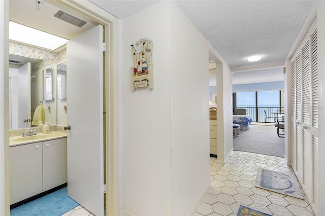 14950 Gulf Blvd Unit 905, Madeira Beach, FL 33708 - corridor featuring a textured ceiling, a sink, a water view, baseboards, and light tile patterned floors