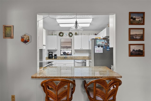 1633 Bentwood Dr, Sun City Center, FL 33573 - kitchen with appliances with stainless steel finishes, a peninsula, a breakfast bar area, white cabinets, and light stone countertops