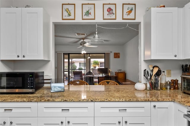 1633 Bentwood Dr, Sun City Center, FL 33573 - kitchen with a ceiling fan, white cabinetry, light stone counters, and a textured ceiling