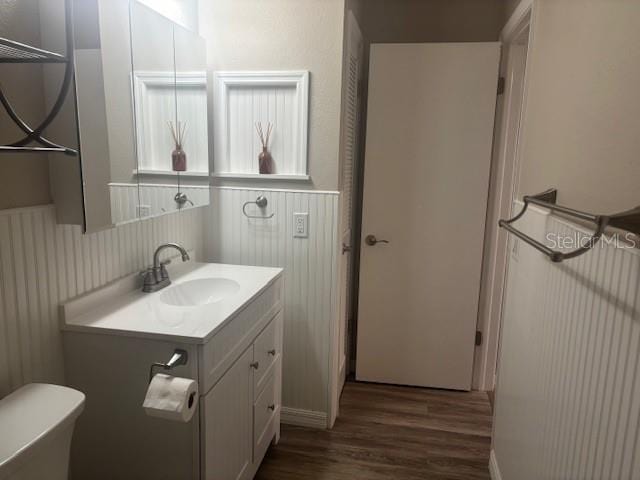 6520 Thicket Trl, New Port Richey, FL 34653 - half bathroom featuring wood finished floors, vanity, wainscoting, and toilet