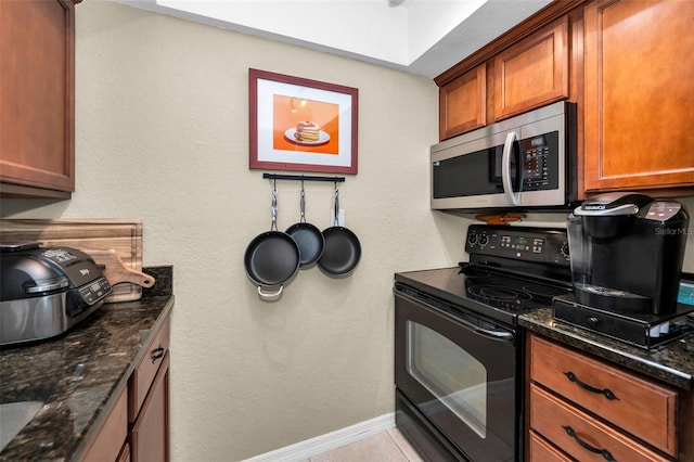 704 Lyndhurst St Unit 624, Dunedin, FL 34698 - kitchen with stainless steel microwave, black electric range, brown cabinetry, dark stone countertops, and baseboards