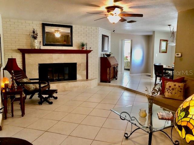 14530 Apache Ave, Largo, FL 33774 - tiled living area with a ceiling fan, a fireplace, and brick wall