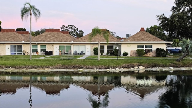 4324 Tahitian Gardens Cir Unit J, Holiday, FL 34691 - back of property at dusk featuring a yard, a water view, stucco siding, and a chimney