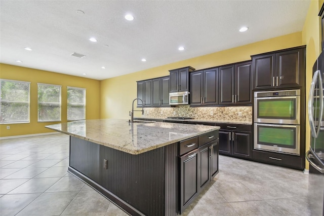 4089 Windcrest Dr, Wesley Chapel, FL 33544 - kitchen featuring a sink, stainless steel appliances, an island with sink, tasteful backsplash, and light stone countertops