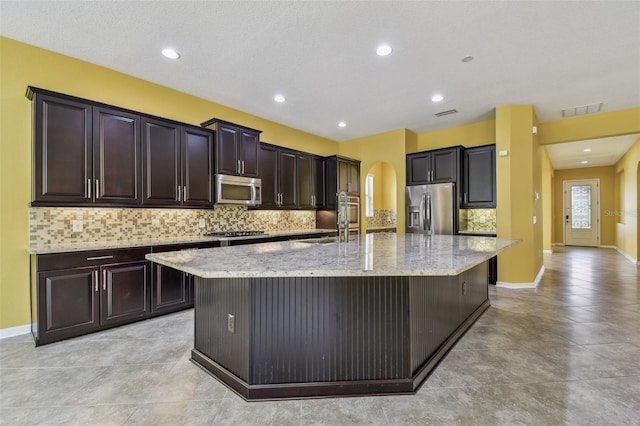 4089 Windcrest Dr, Wesley Chapel, FL 33544 - kitchen with stainless steel appliances, arched walkways, a spacious island, tasteful backsplash, and light stone countertops
