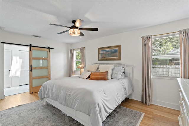 125 Live Oak Ln, Largo, FL 33770 - bedroom with light wood-style floors, baseboards, a barn door, ceiling fan, and a textured ceiling