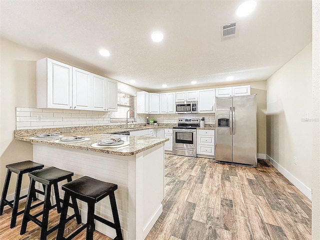 1025 Reading Rd, Lutz, FL 33558 - kitchen featuring appliances with stainless steel finishes, a peninsula, backsplash, light wood finished floors, and white cabinetry