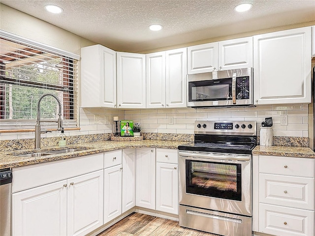 1025 Reading Rd, Lutz, FL 33558 - kitchen with appliances with stainless steel finishes, a sink, light wood finished floors, a textured ceiling, and white cabinets