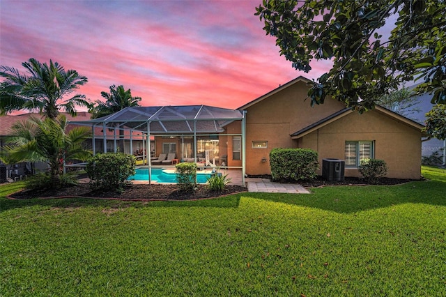 4133 Auston Way, Palm Harbor, FL 34685 - back of house at dusk featuring stucco siding, central air condition unit, a patio, a lawn, and an outdoor pool