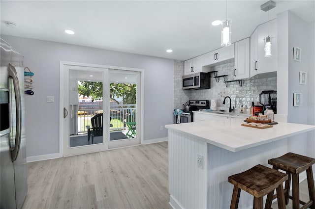 13325 1st St E, Madeira Beach, FL 33708 - kitchen featuring appliances with stainless steel finishes, a sink, light wood-style floors, backsplash, and a kitchen bar