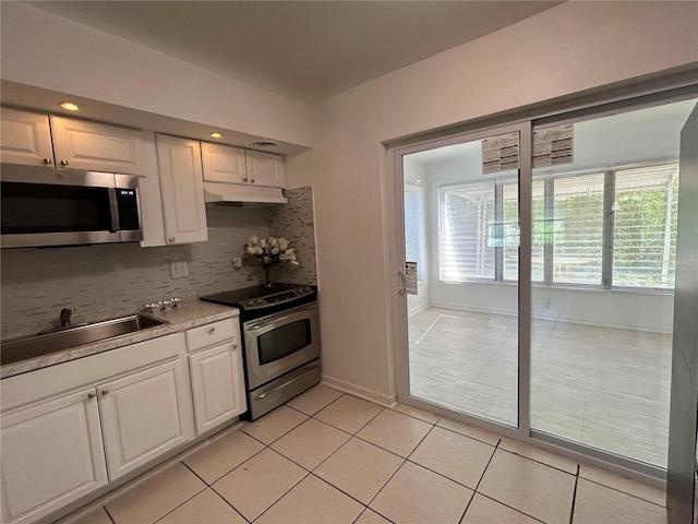 7313 Royal Palm Dr, New Port Richey, FL 34652 - kitchen with stainless steel appliances, under cabinet range hood, white cabinetry, tasteful backsplash, and light tile patterned floors