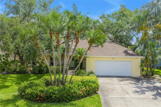 8127 Siquita Dr NE, Saint Petersburg, FL 33702 - obstructed view of property featuring roof with shingles, driveway, stucco siding, a garage, and a front yard