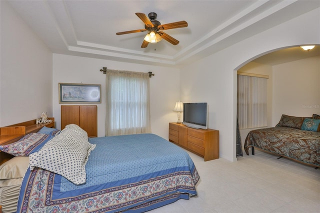 2128 Worthington Greens Dr, Sun City Center, FL 33573 - bedroom featuring arched walkways, a tray ceiling, a ceiling fan, and tile patterned flooring