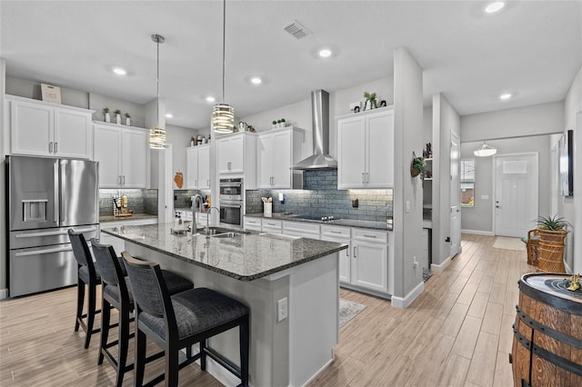 31921 Magna Gulf Loop, San Antonio, FL 33576 - kitchen with stainless steel appliances, wall chimney range hood, a sink, a kitchen bar, and light wood-style floors