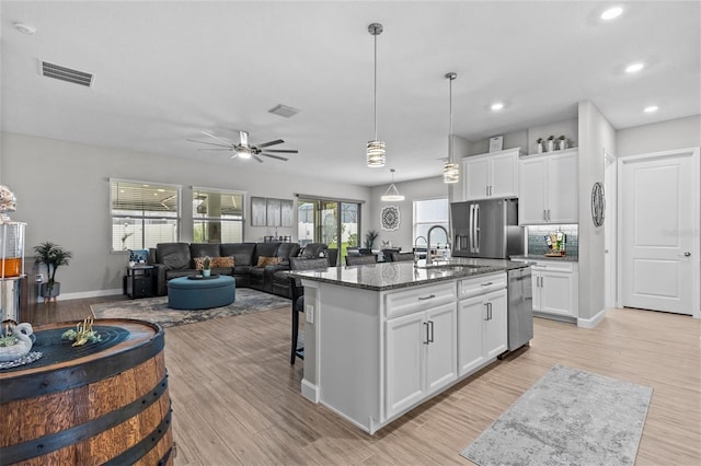 31921 Magna Gulf Loop, San Antonio, FL 33576 - kitchen featuring appliances with stainless steel finishes, a sink, dark stone counters, a kitchen island with sink, and light wood finished floors
