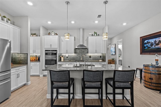 31921 Magna Gulf Loop, San Antonio, FL 33576 - kitchen featuring wall chimney exhaust hood, appliances with stainless steel finishes, a sink, tasteful backsplash, and a breakfast bar