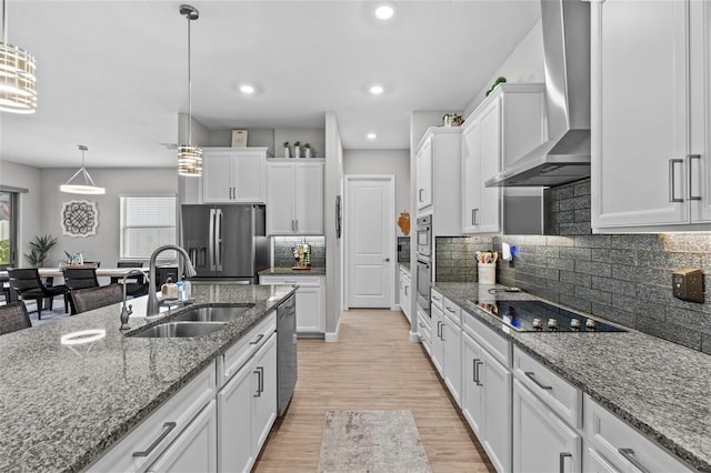 31921 Magna Gulf Loop, San Antonio, FL 33576 - kitchen with wall chimney range hood, stainless steel appliances, a sink, white cabinets, and light wood-style flooring