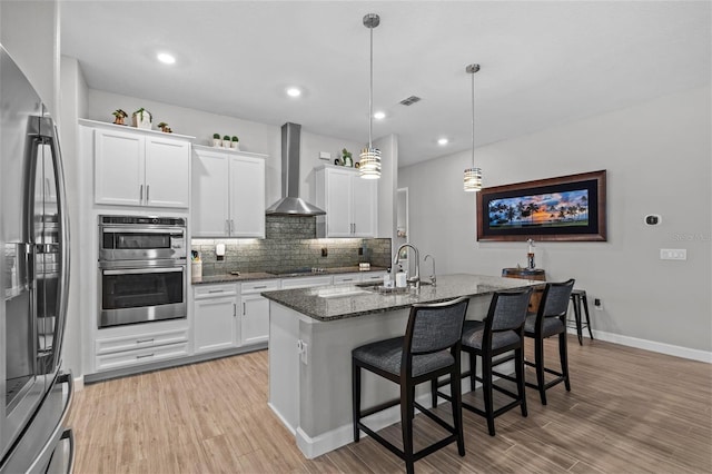 31921 Magna Gulf Loop, San Antonio, FL 33576 - kitchen with wall chimney exhaust hood, a sink, appliances with stainless steel finishes, dark stone countertops, and light wood-style floors