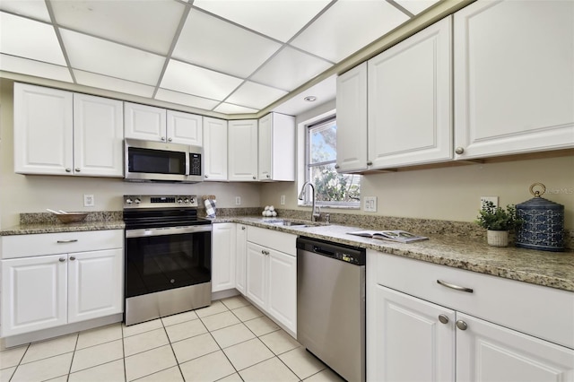 5825 Oakhurst Dr, Seminole, FL 33772 - kitchen with stainless steel appliances, a sink, white cabinetry, light tile patterned flooring, and light stone countertops
