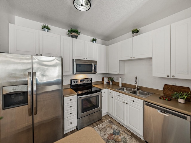 4221 W Spruce St Unit 2302, Tampa, FL 33607 - kitchen with appliances with stainless steel finishes, a sink, a textured ceiling, white cabinetry, and wood finished floors