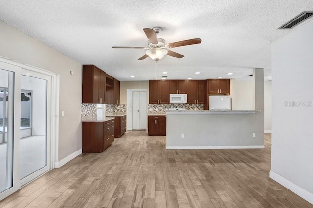 3917 Casaba Loop, Valrico, FL 33596 - kitchen with fridge, white microwave, light wood-style flooring, ceiling fan, and decorative backsplash