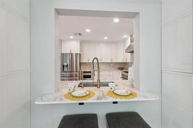 1709 Main St, Safety Harbor, FL 34695 - kitchen featuring appliances with stainless steel finishes, a sink, decorative backsplash, white cabinets, and wall chimney range hood